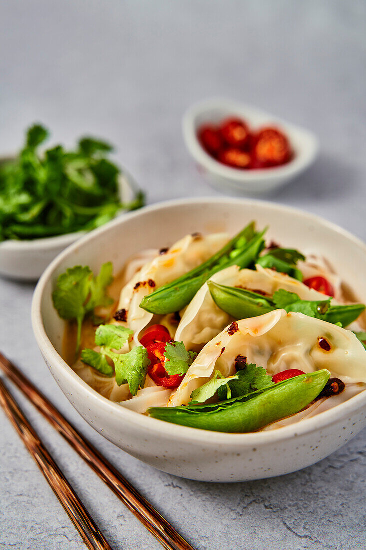 Vegetable gyoza noodles with sugar snaps, coriander and chilli on a grey surface