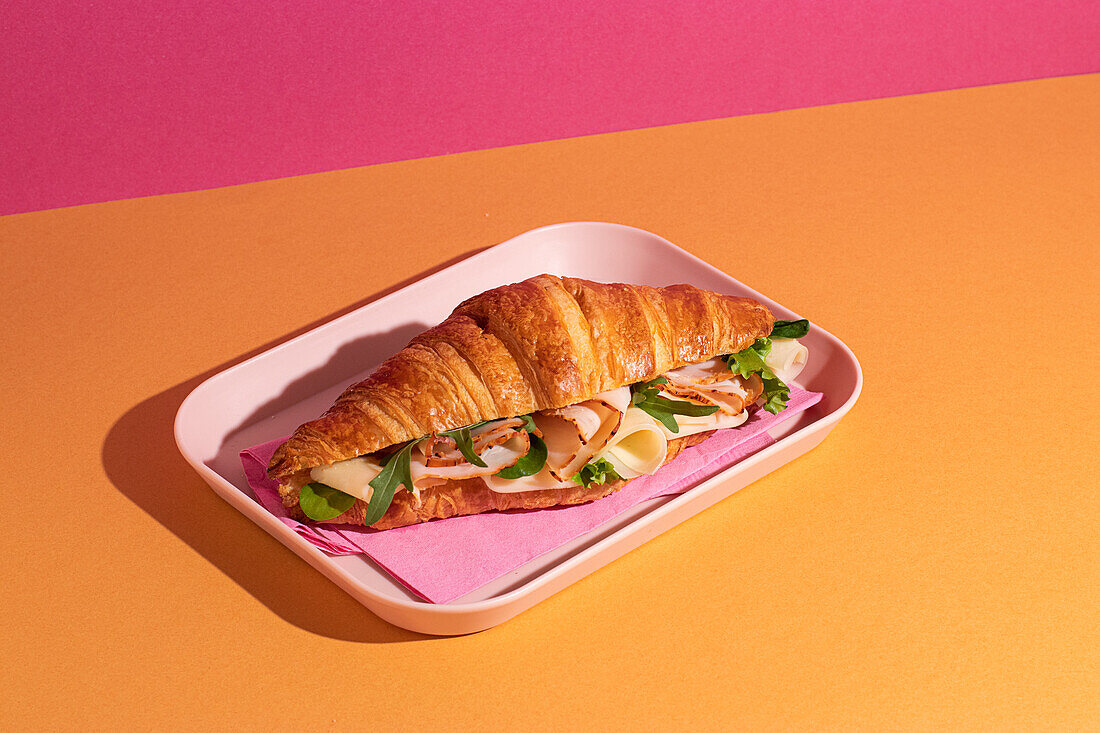 From above of delicious croissant with ham, cheese and rocket leaves placed on plate in colorful background