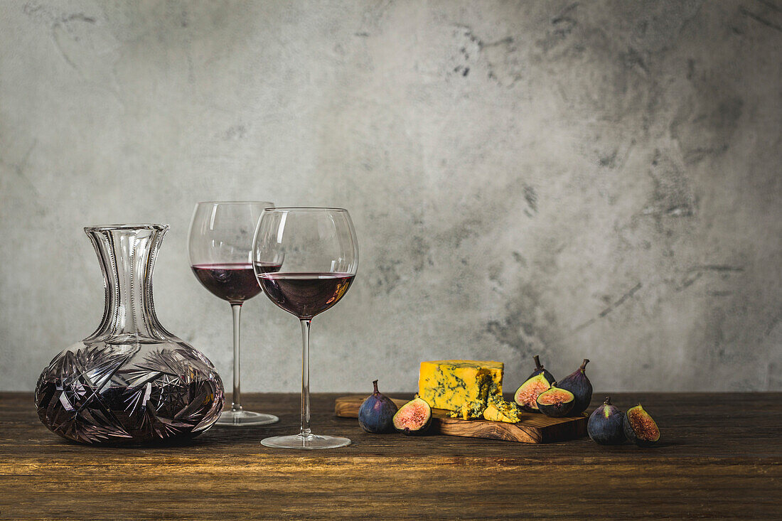 Rotwein in zwei Stielgläsern und Kristallkaraffe mit Blauschimmelkäse und Feigen