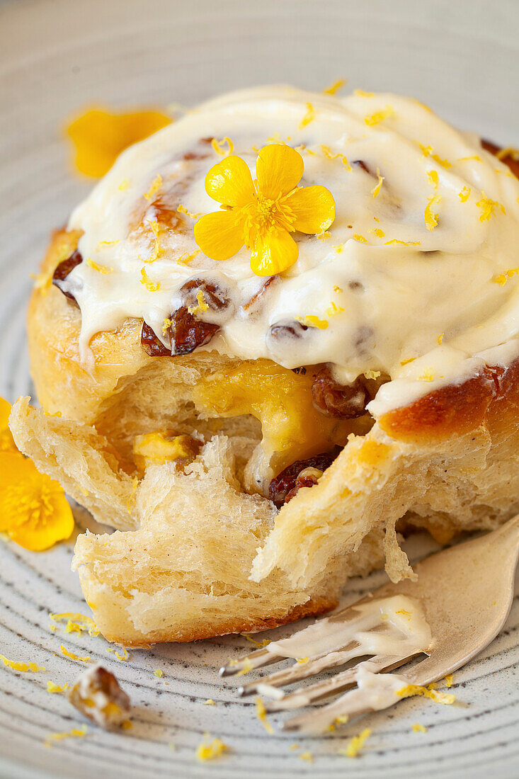 A lemon roll filled with lemon curd, dried fruit and pistachios, topped with cream cheese on a plate