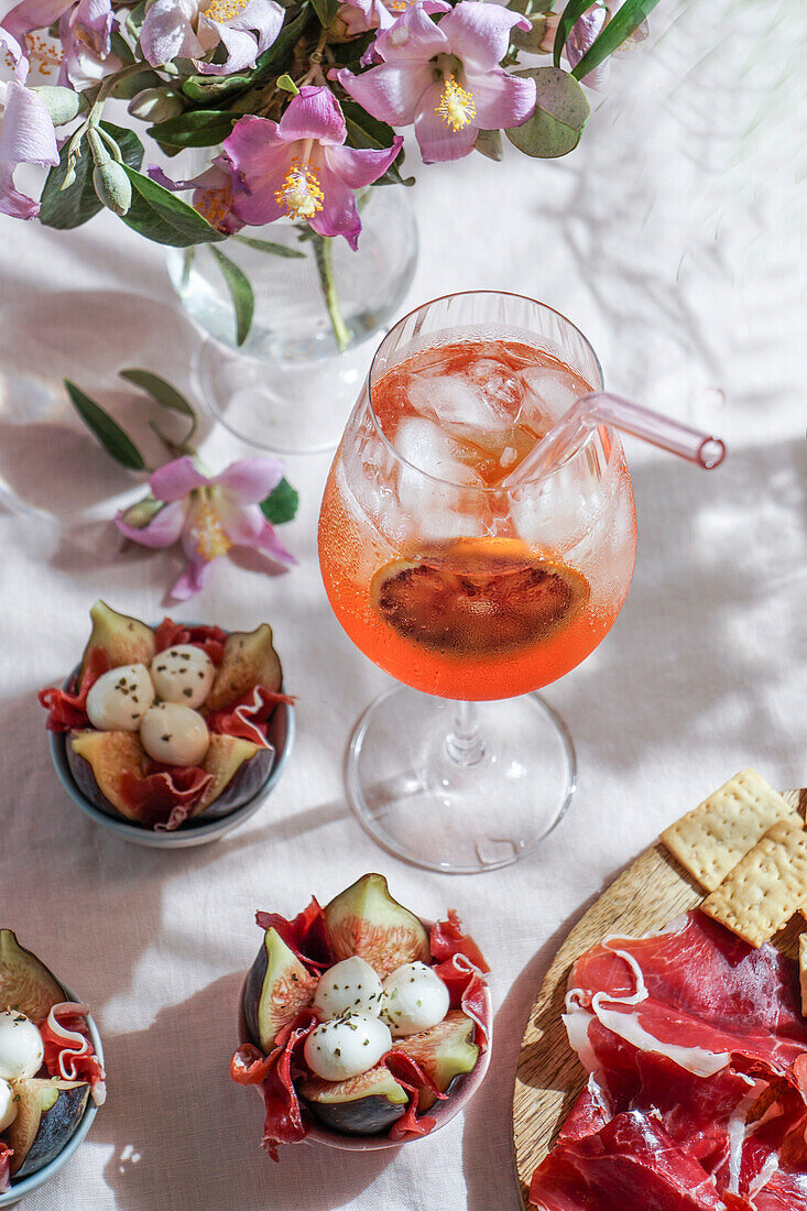 Aperol Spritz-Cocktail, auf zartrosa Leinentischdecke, Schatten, Sonnenlicht, Sommerdrink im Glas