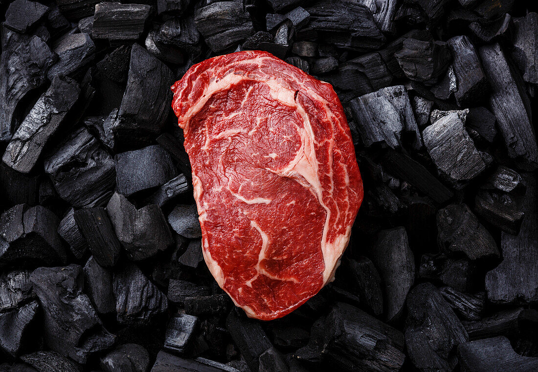 Rohes Frischfleisch Ribeye-Steak auf schwarzem Holzkohle-Hintergrund