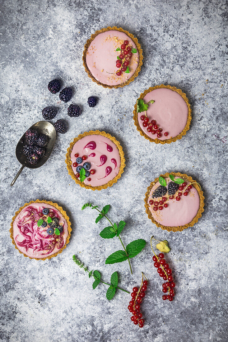 Arrangement of four small tarts filled with berry cream, decorated with fresh fruit and mint