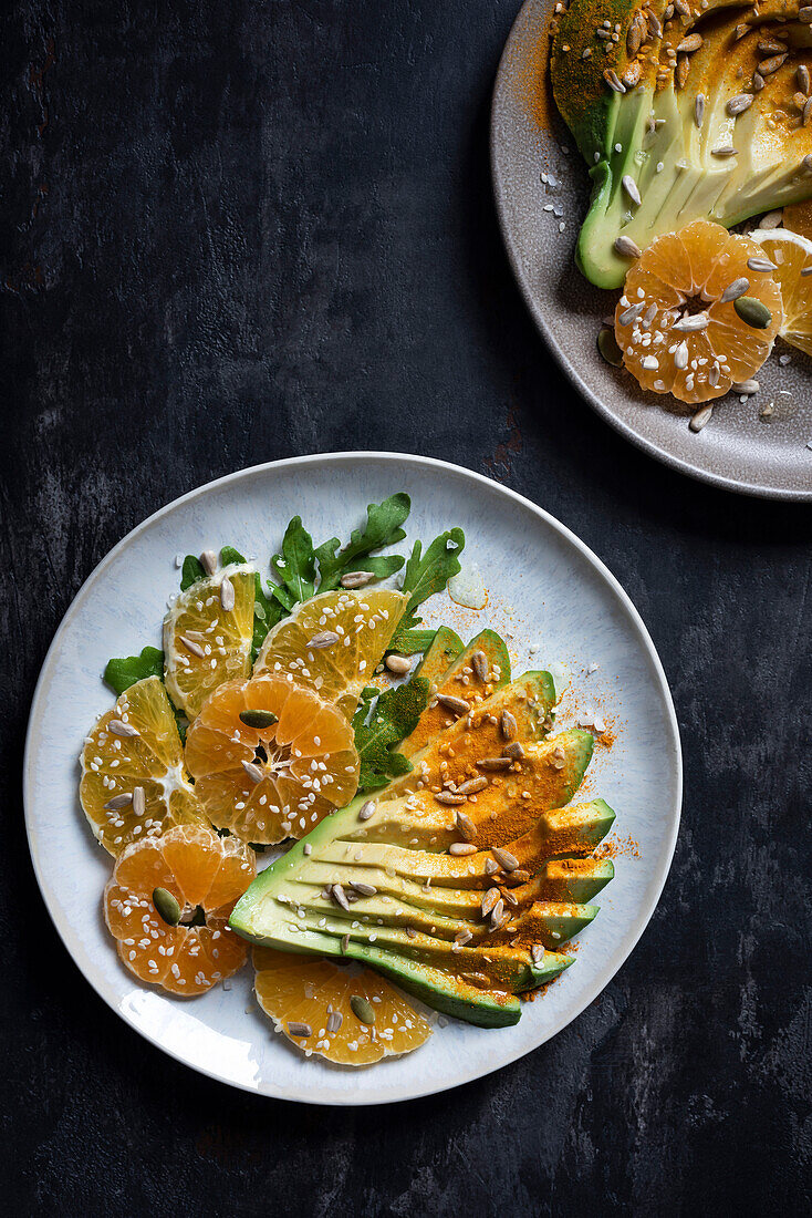 Two salads with avocado, tangerines, oranges, arugula and various grains on a dark background. Top view.