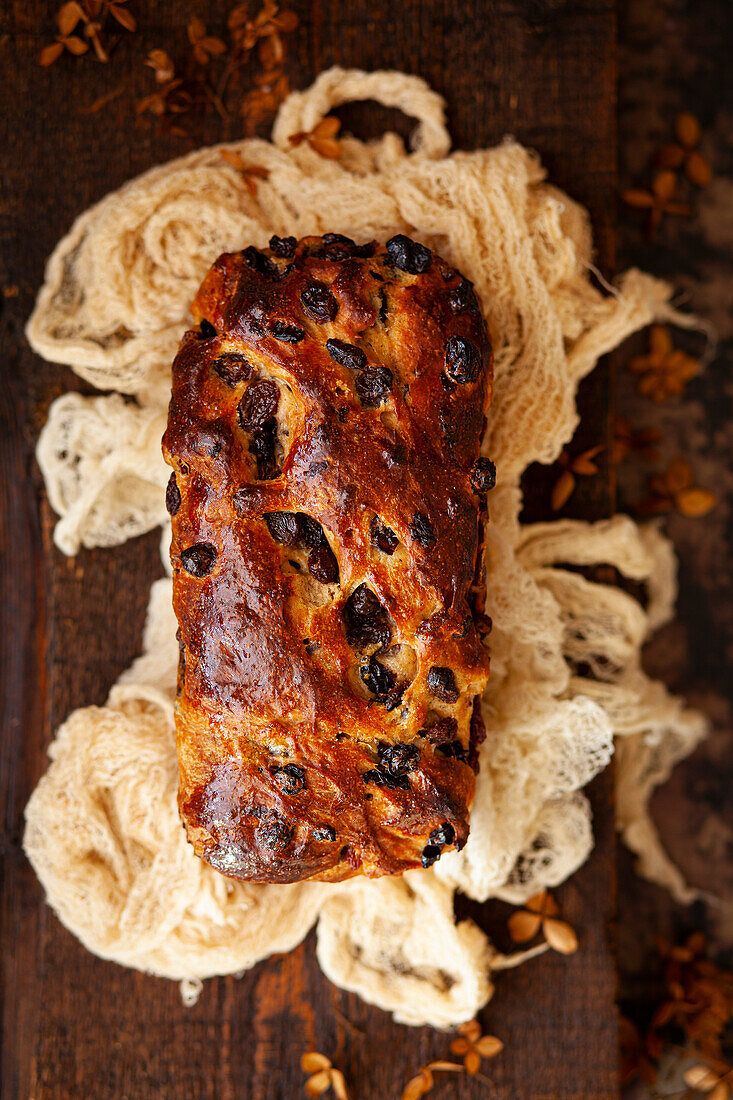 A whole, unsliced fruit loaf on a cloth in a rustic setting