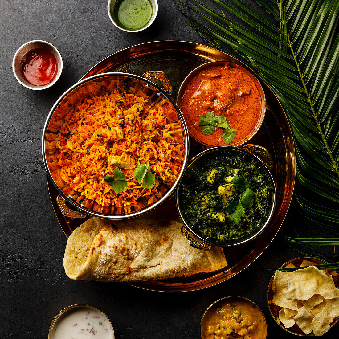 Indisches Essen Chicken Biryani, Curry-Butter-Huhn, Palak Paneer, Papad, Dal und Naan-Brot auf dunklem Hintergrund