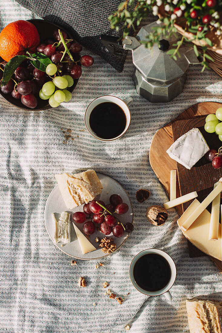 Picknickszene mit Kaffee und Teller mit Weintrauben, Käse und Baguette