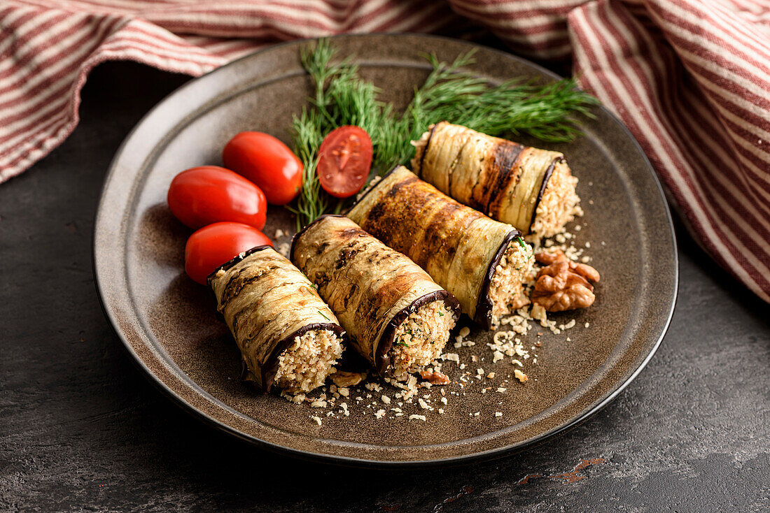 Grilled aubergine rolls with walnut filling on a plate with tomatoes and fresh green dill