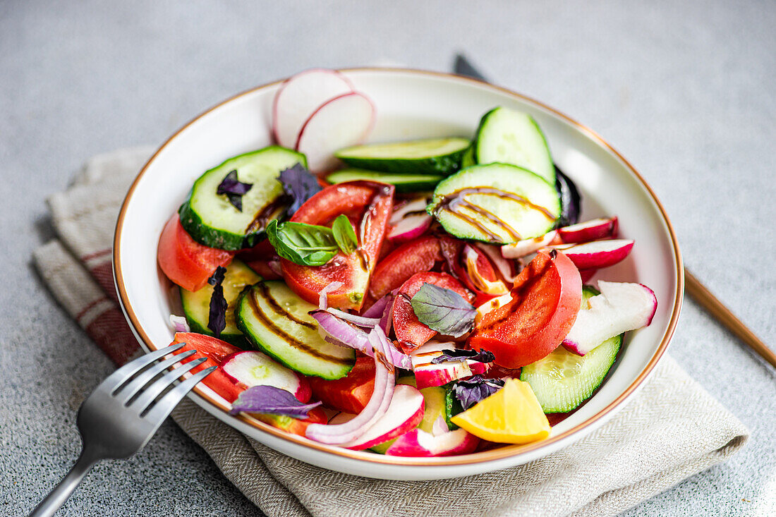 Hochformatiger, schmackhafter vegetarischer Salat mit Gurke, Zitrone, Zwiebel und Tomate mit grünen Blättern und Dressing in einer Schale auf dem Tisch
