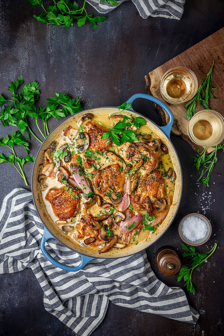 Chicken in wine cream sauce with mushrooms, shallots and parsley in a blue enamelled pot with napkin