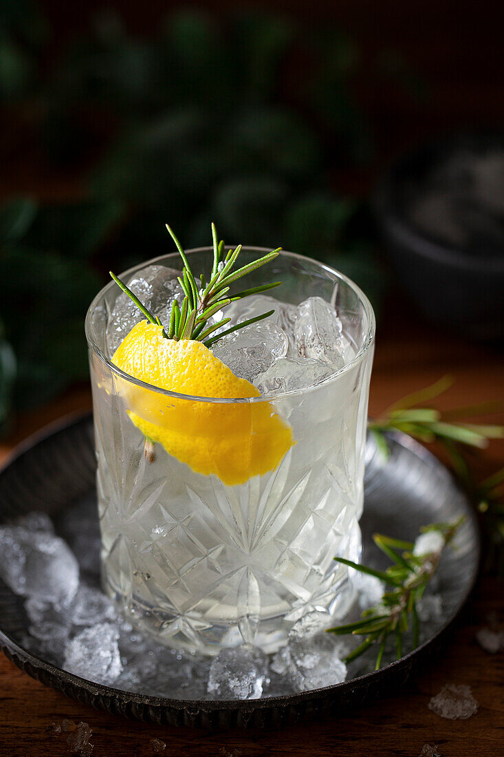 A white Negroni Bianco cocktail with lemon and rosemary herb garnish