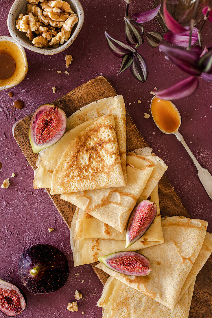 Crepes, folded on a handmade ceramic plate, decorated with figs, caramel and walnuts on a purple background