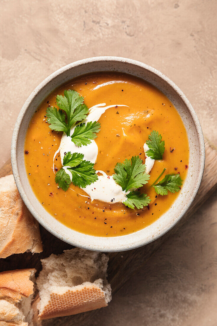 Butternusskürbissuppe und Baguette auf Holzbrett