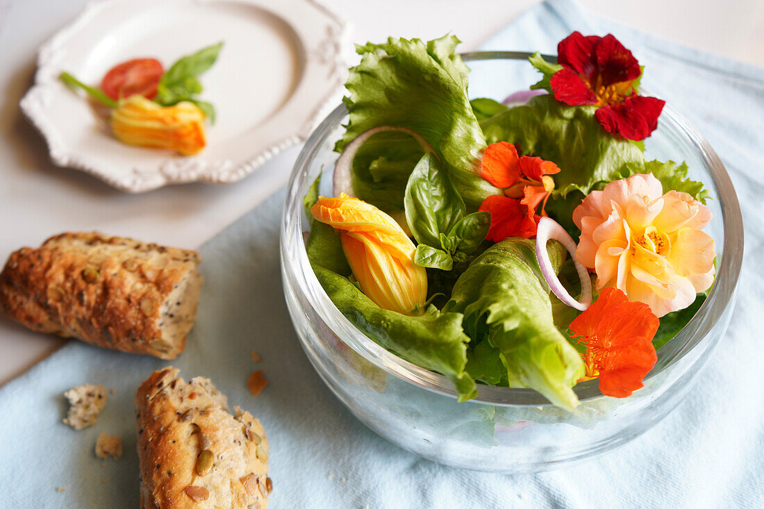 Mediterranean salad with zucchini, nasturtium, and rose edible flowers lunchtime table setting, top down closeup. Horizontal orientation.