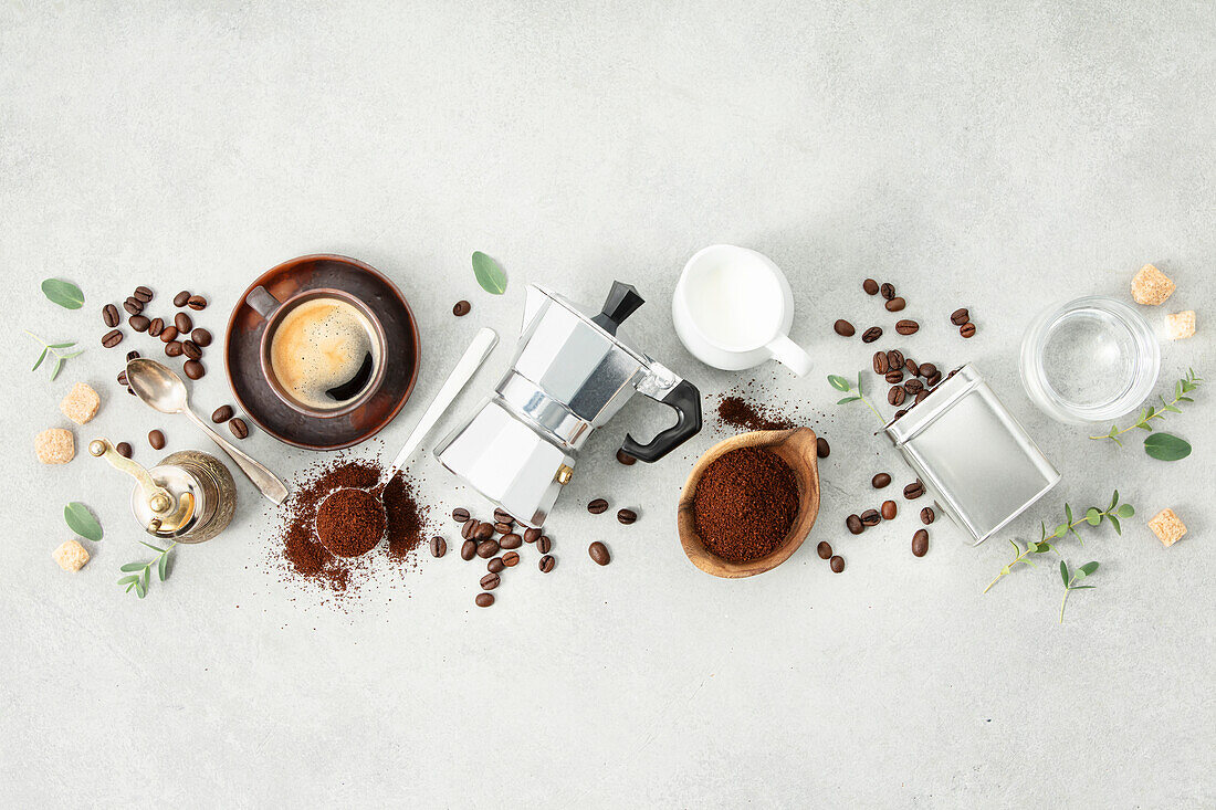 Flat lay with Moka pot, espresso cup, ground coffee, milk, sugar and coffee beans on a grey concrete background. Header with brewing coffee ingredients.