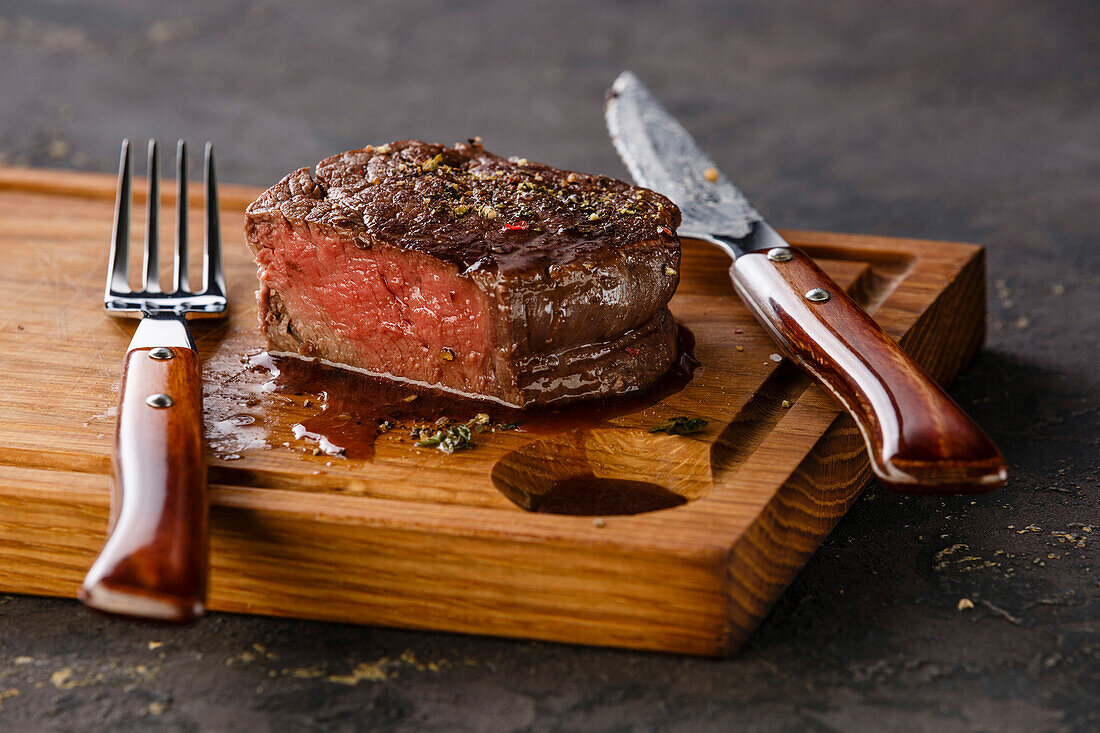 Filet mignon steak on a wooden board against a black background