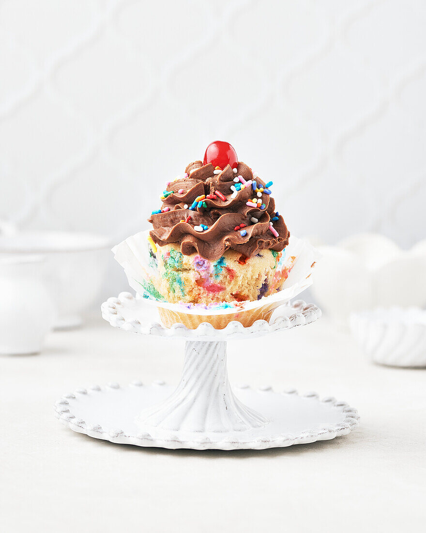 Vegan and gluten-free funfetti cupcake with chocolate funfetti icing and maraschino cherry