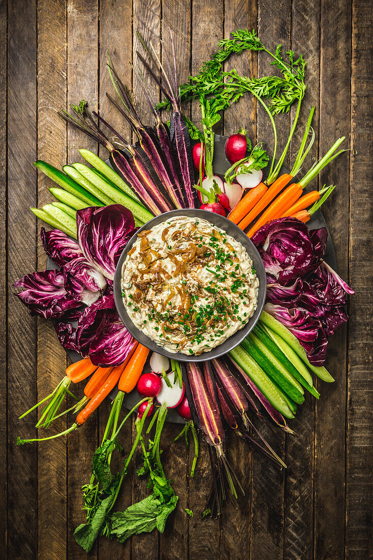 Top view of an onion dip in a bowl surrounded by fresh, colourful vegetables on a wooden background