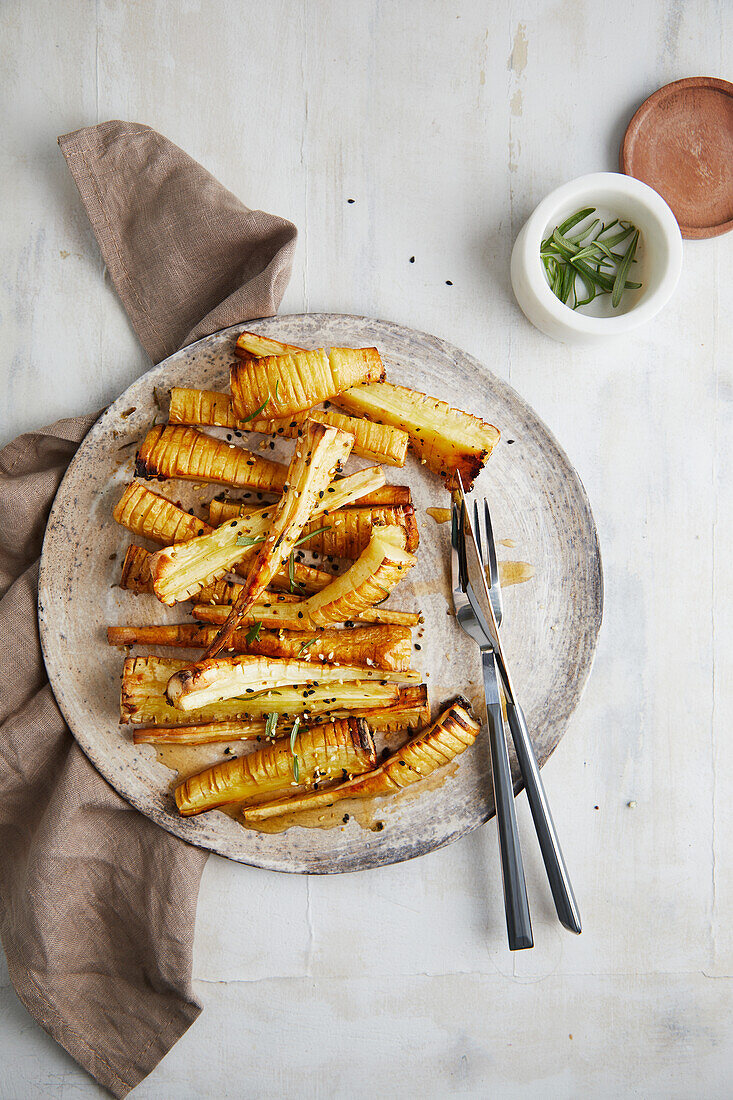 Top view of delicious baked parsnip sticks, served on a plate with rosemary and sesame seeds on a white table in the kitchen