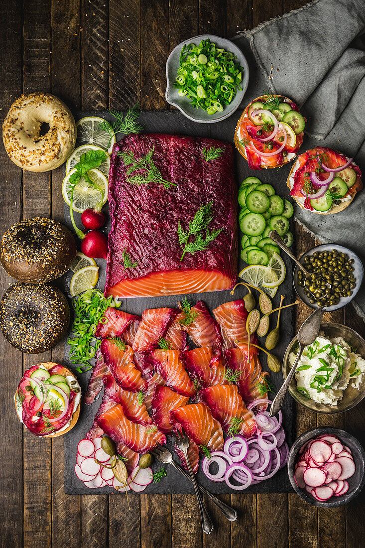 Brunch spread with Beet-cured Salmon, bagels , cream cheese, and garnishes on slate board