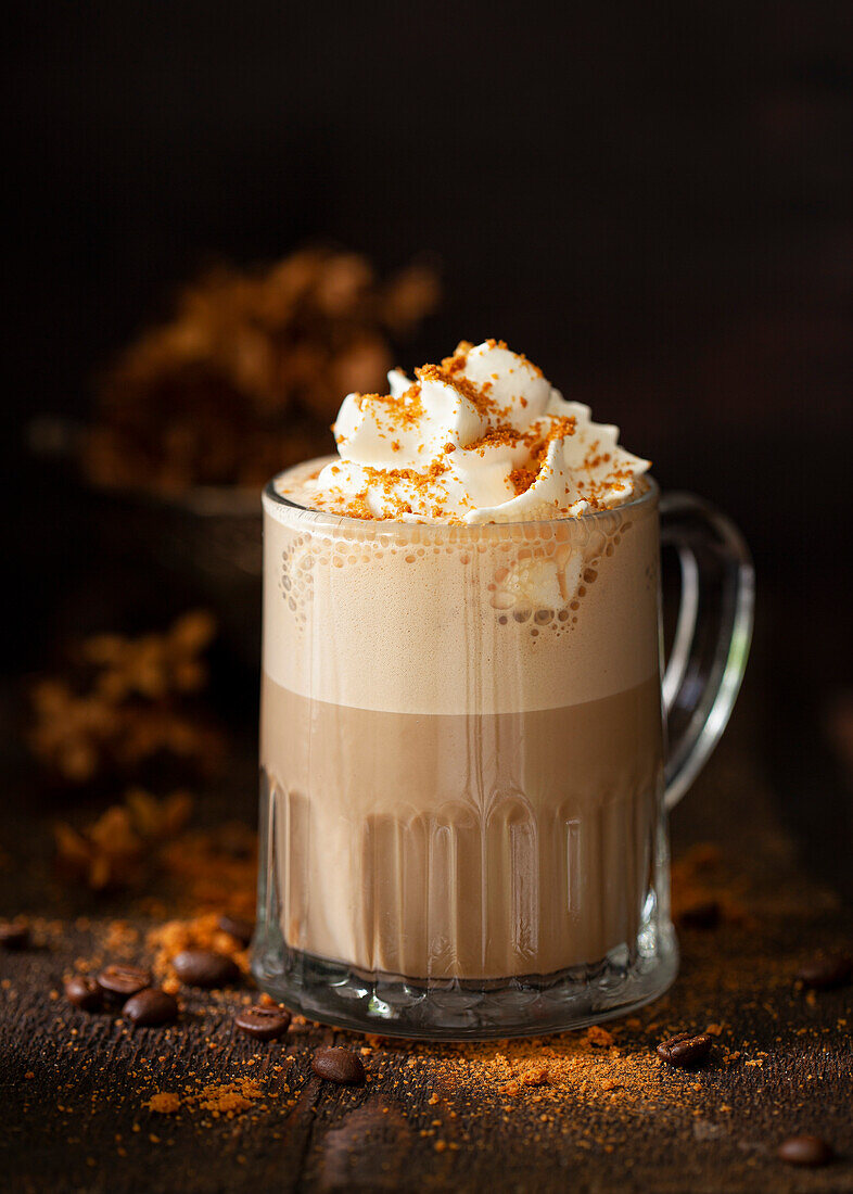 A sweet latte coffee drink topped with whipped cream and cookie crumbs in a dark and moody rustic setting.