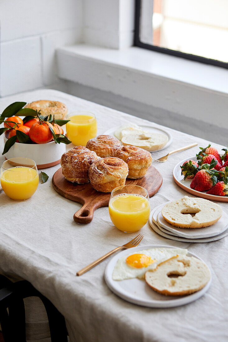 Frühstückstischlandschaft mit Gebäck, Orangensaft und Obst