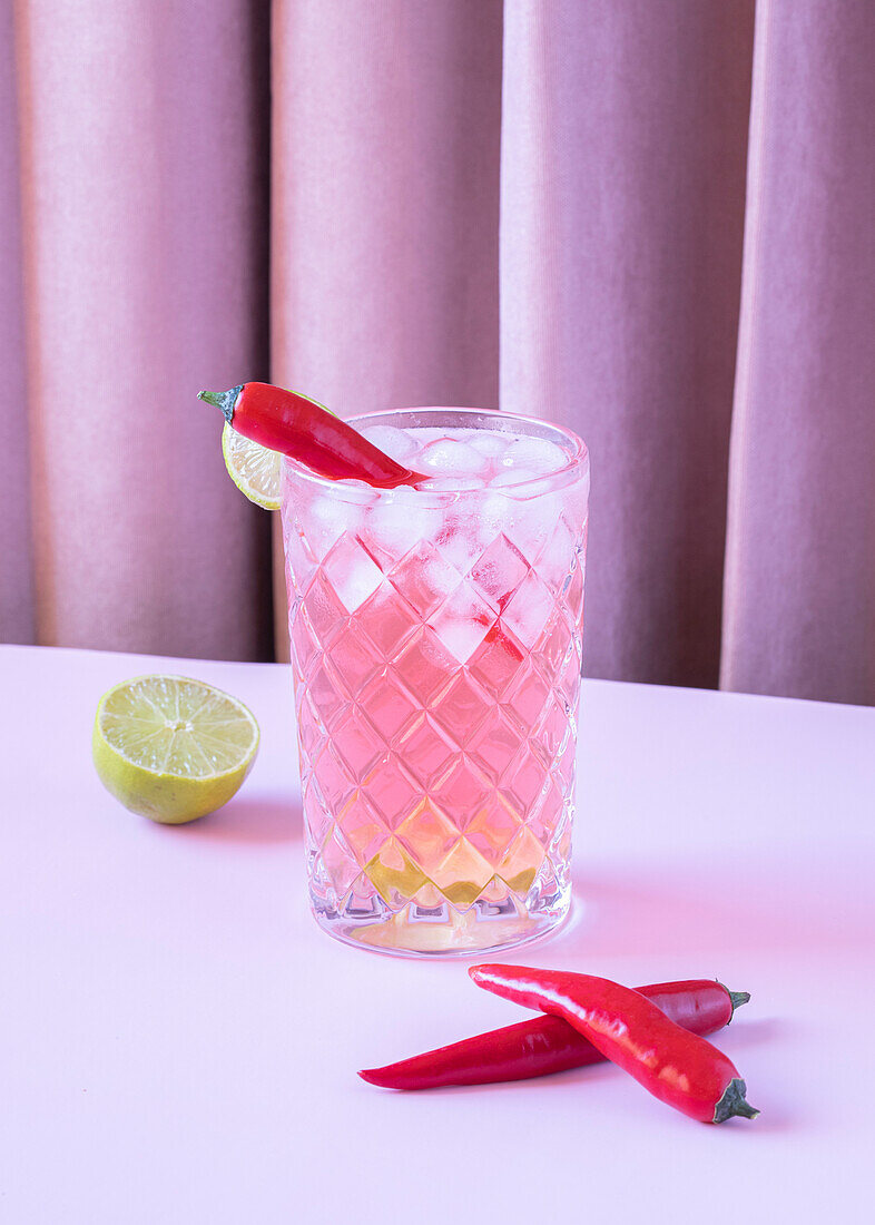 Clear glass filled with chilled refreshing cocktail served with pepper and ice cubes placed on the table with lime and peppers