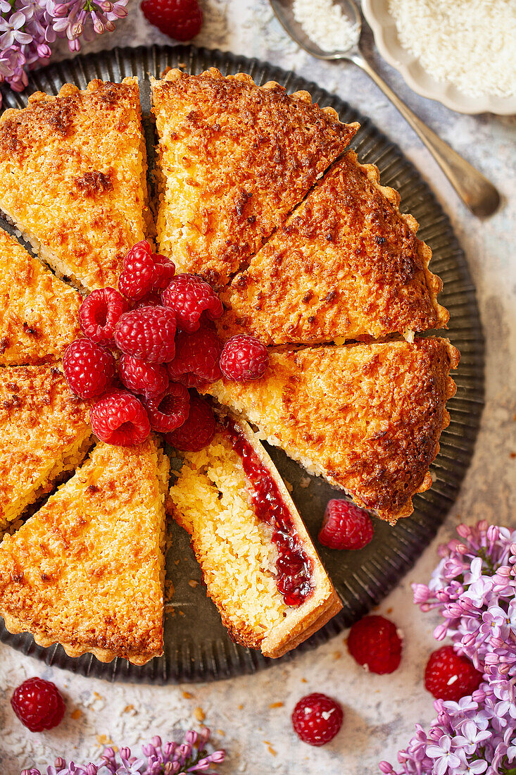 A raspberry and coconut tart with a pile of fresh raspberries in the centre