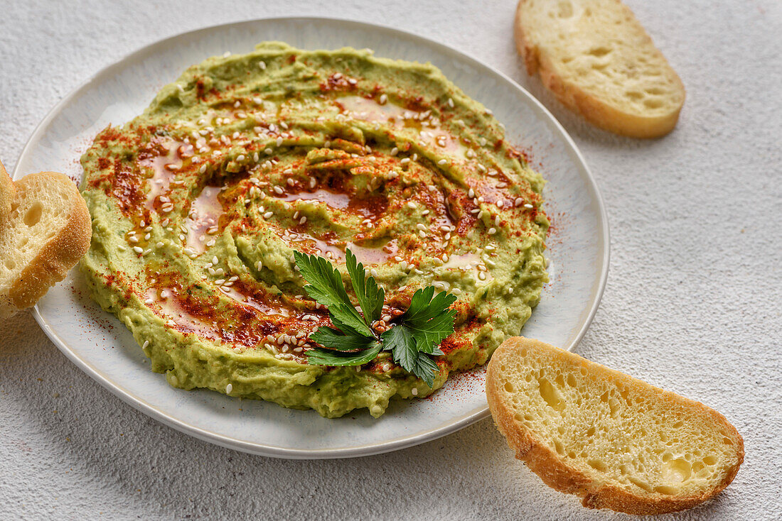 Avocado hummus flavoured with sesame seeds, paprika and parsley. The dish is served with toast