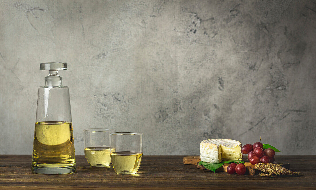 Weißwein in stiellosen Gläsern und moderner Karaffe mit Briekäse und Trauben