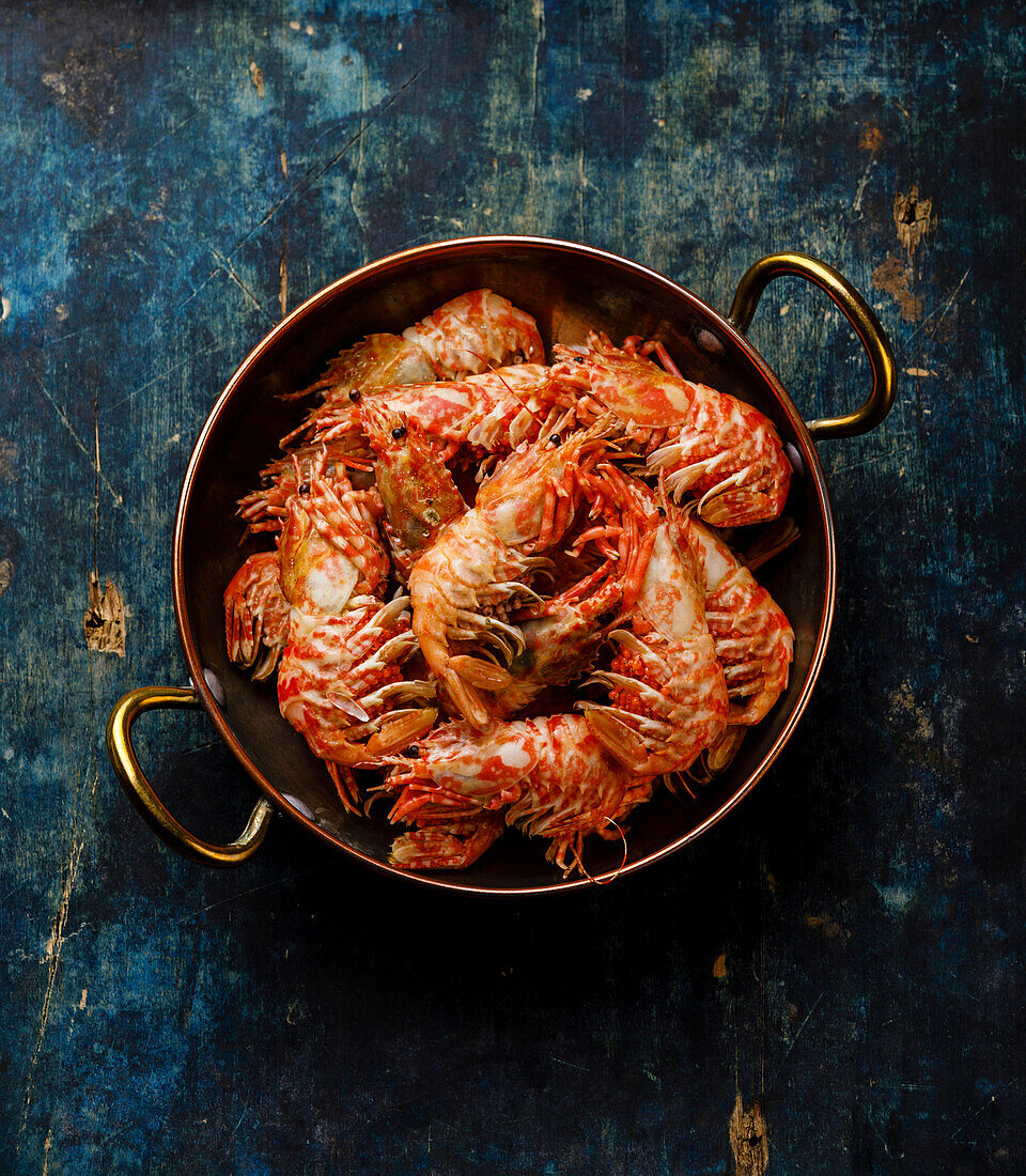 Cooked pink Greenland prawn in copper pan on blue background