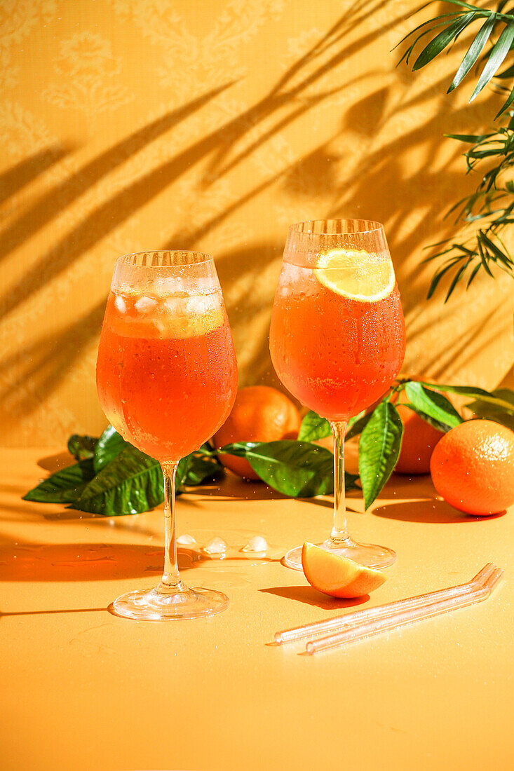 Aperol Spritz cocktail with ice, a misted refreshing drink, on an orange background, sunlight, shadow, a summer drink in a wine glass