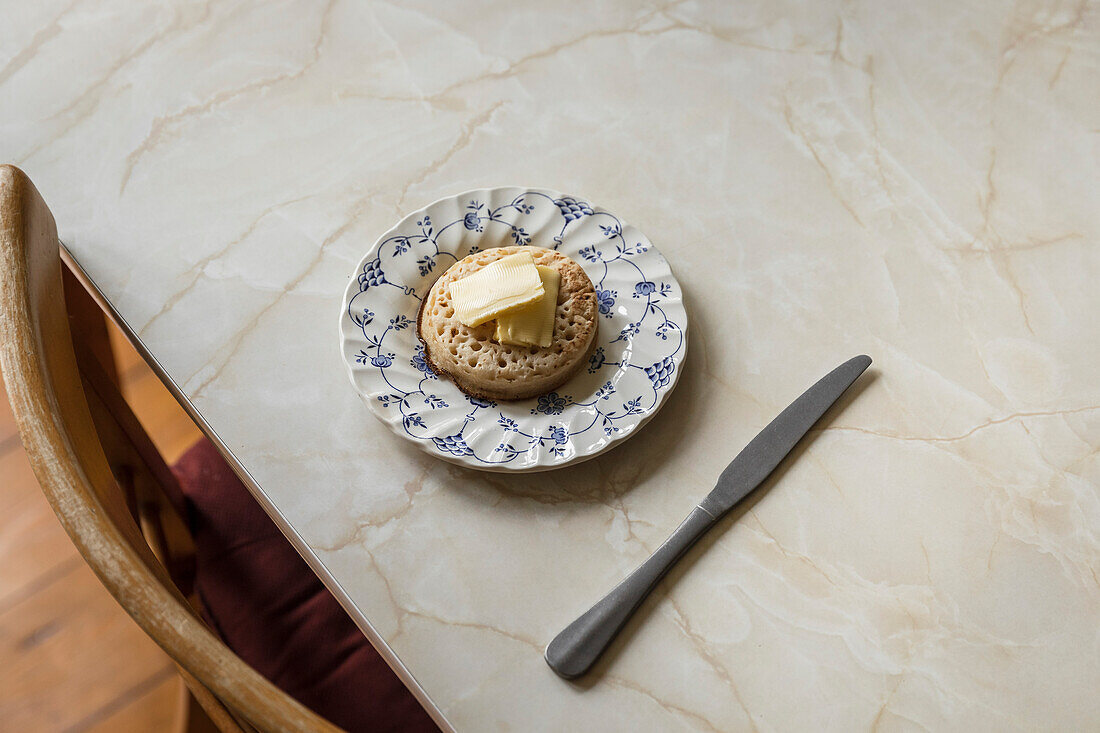 Crumpet with butter on a blue flower plate on a marble table