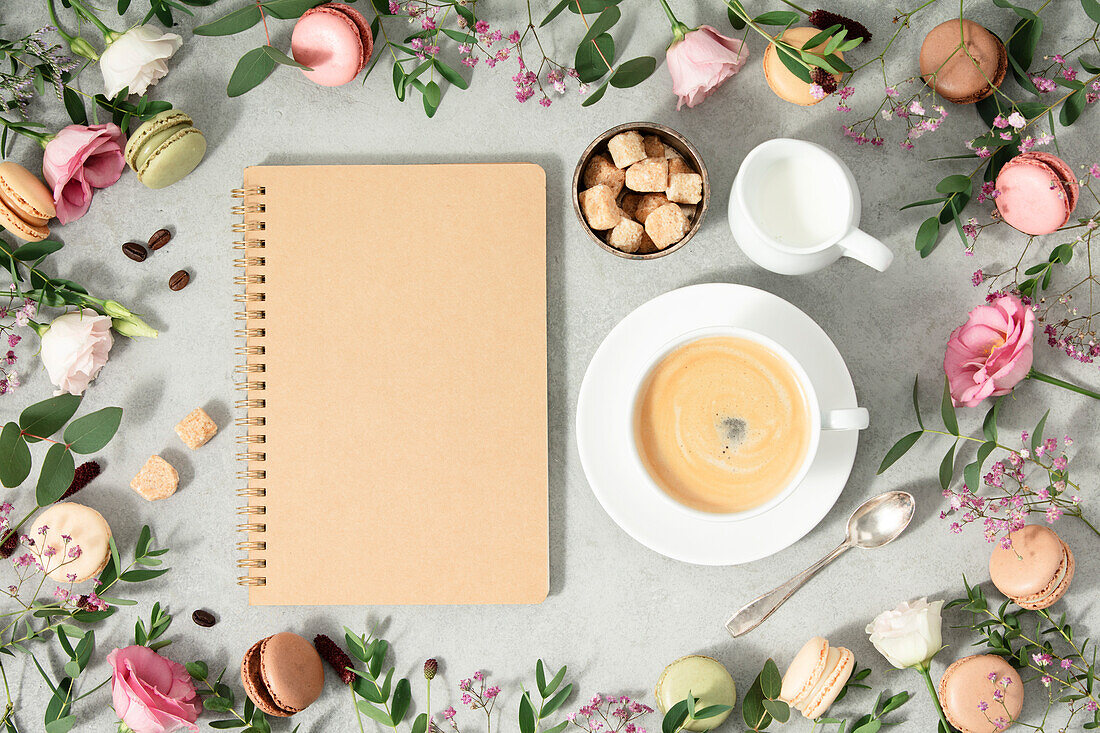 White coffee cup, blank notebook and frame made of spring flowers and different types of macaroons Flat Lay Mock Up Copy Space