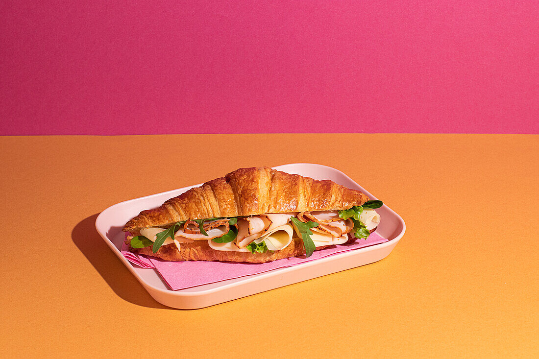Delicious croissant with ham, cheese and rocket on a plate with a colourful background from above