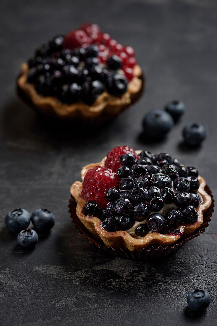 Gebäckkorb mit Heidelbeeren und Himbeeren. Torte auf dunklem Hintergrund