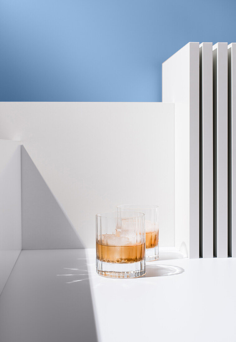 Front view of transparent glasses filled with cold, refreshing scotch whiskey with ice cubes on a white surface against a white and blue background