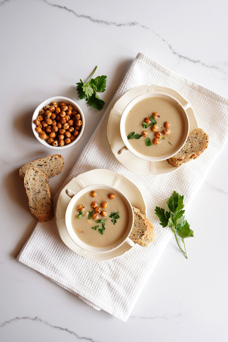 Vegane Suppe aus Blumenkohl, Kreuzkümmel und Limabohnen auf weißer Marmorplatte, serviert in zwei Suppenschalen, Flatlay