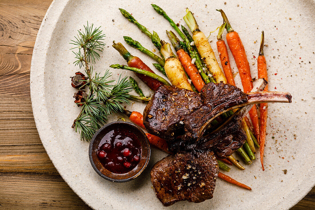 Grilled venison ribs with baked vegetables and berry sauce on a wooden background
