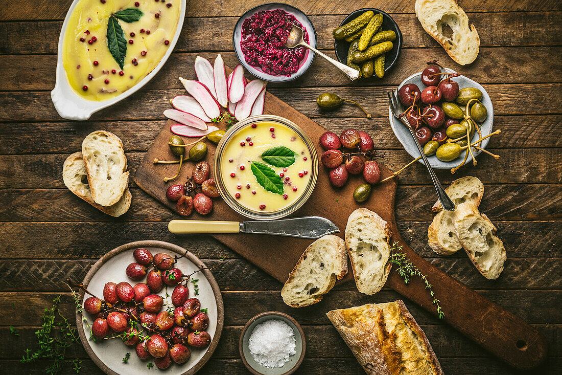 Butter dish on a wooden board with roasted grapes, radishes, cucumber and baguette