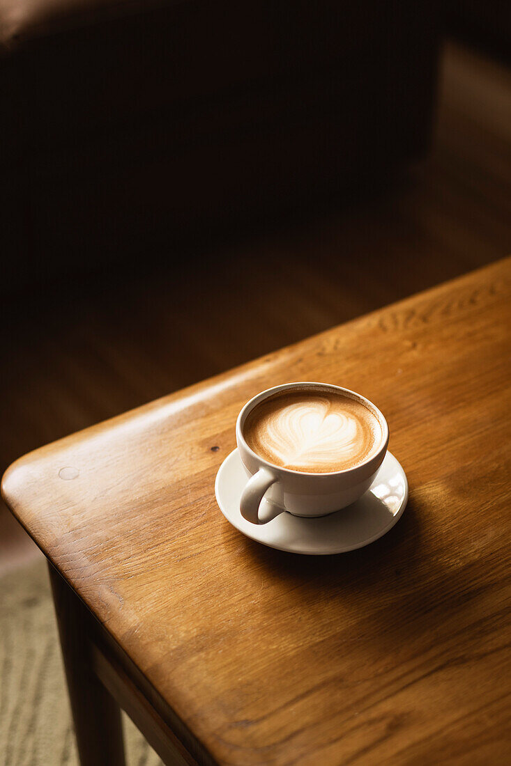 Coffee in white cup on wooden table, with spoon.