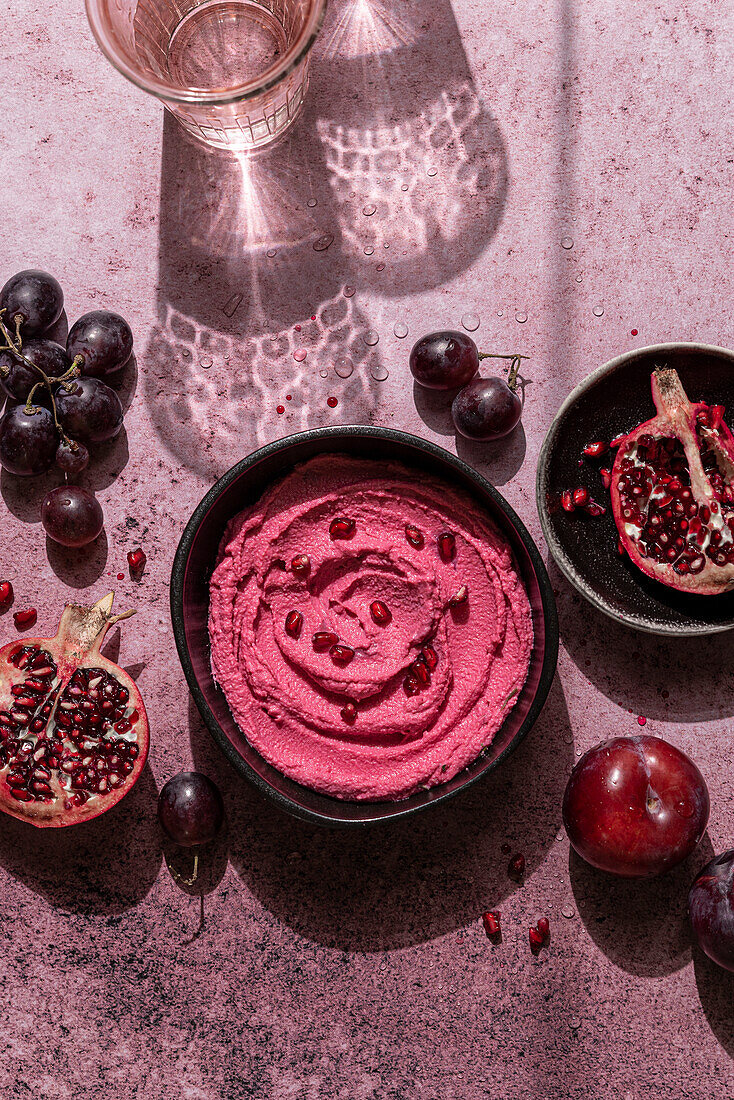 Schale mit rosa Hummus und frischen Früchten in hartem Licht