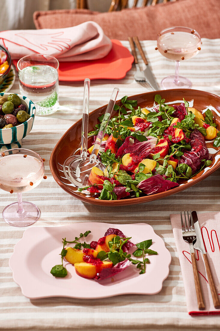 Ein Picknick mit Salat an einem Tisch im Freien, mit frischem Obst und Gebratenem, auf einem gestreiften Tischtuch