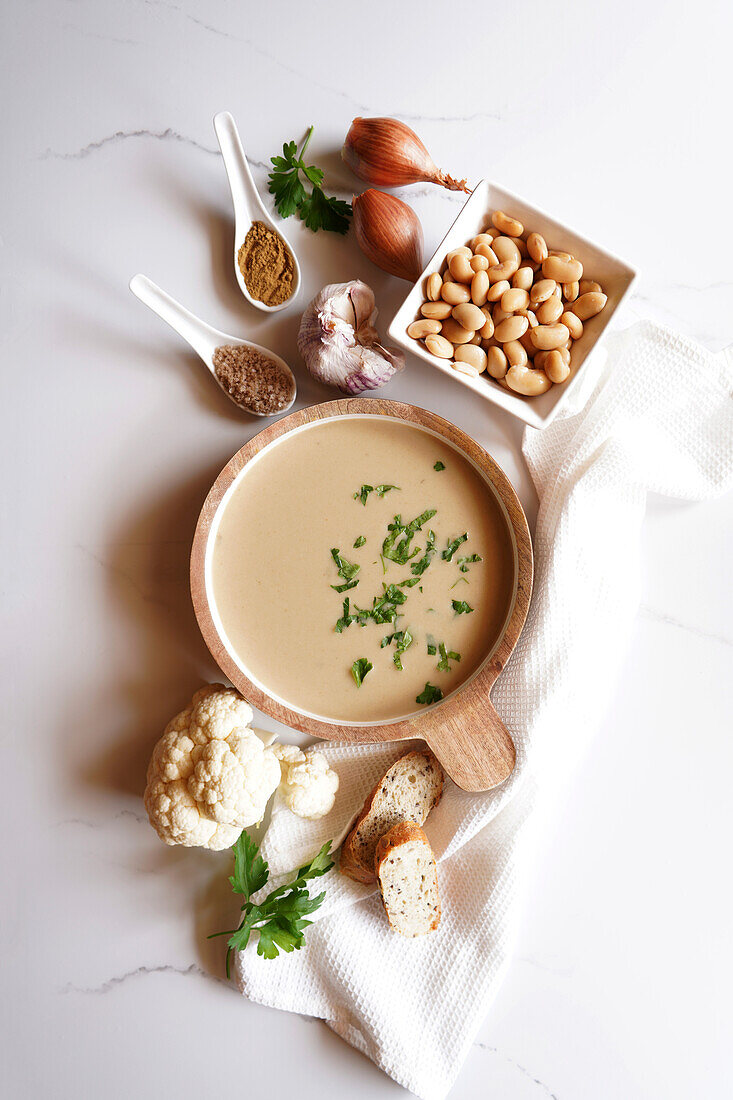 Vegan cauliflower, cumin and lima bean soup with ingredients on a white marble plate Minimal flatlay