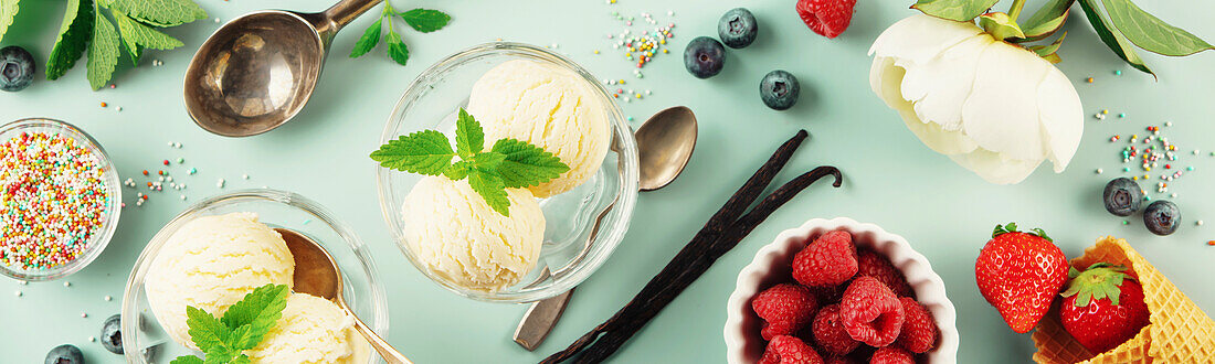 Vanilla balls, mint leaves in glass bowl, sprinkles, berries and flowers on pastel light blue background, top view, banner, copy space. Summery minimal concept