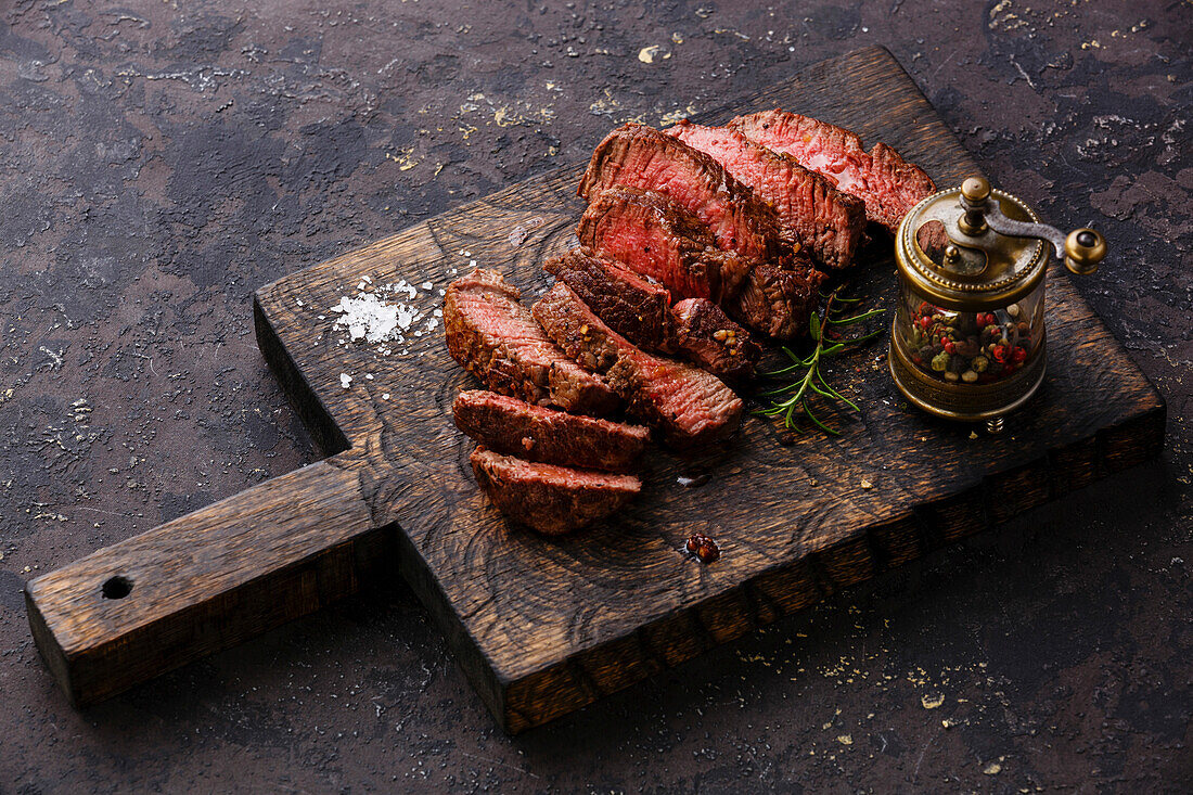 Sliced grilled beef steak and pepper mill on wooden board