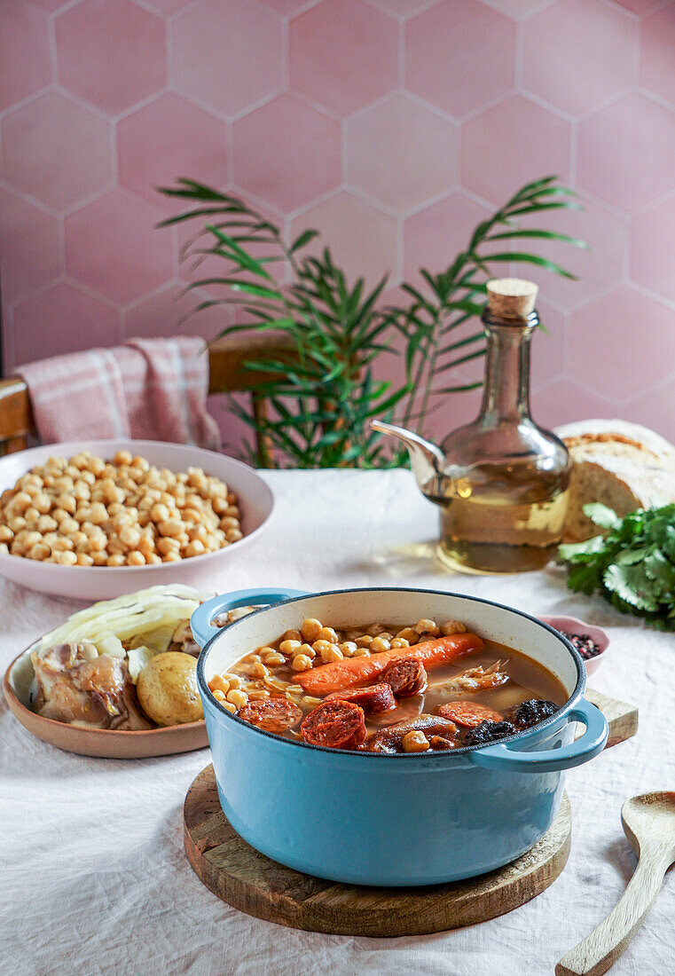 Cocido Madrileño, ein traditionelles spanisches Gericht, ein Eintopf auf Kichererbsenbasis aus Madrid mit rosafarbenen Keramikfliesen im Hintergrund