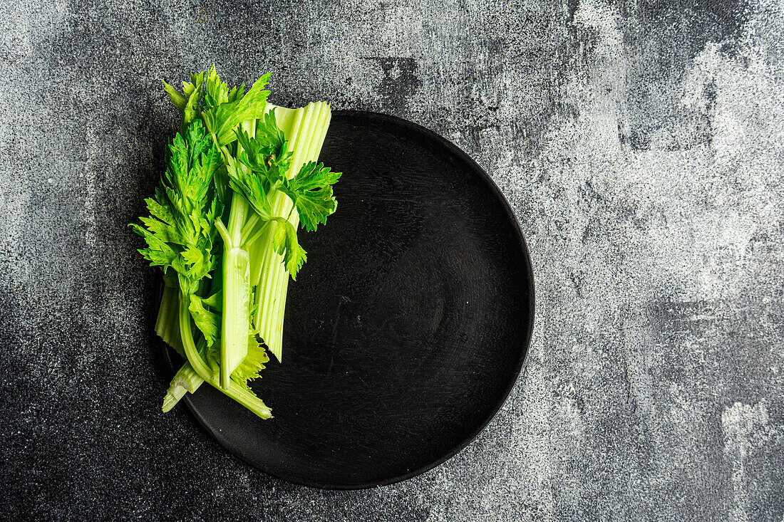 Top view of celery sticks on black plate on concrete grey surface