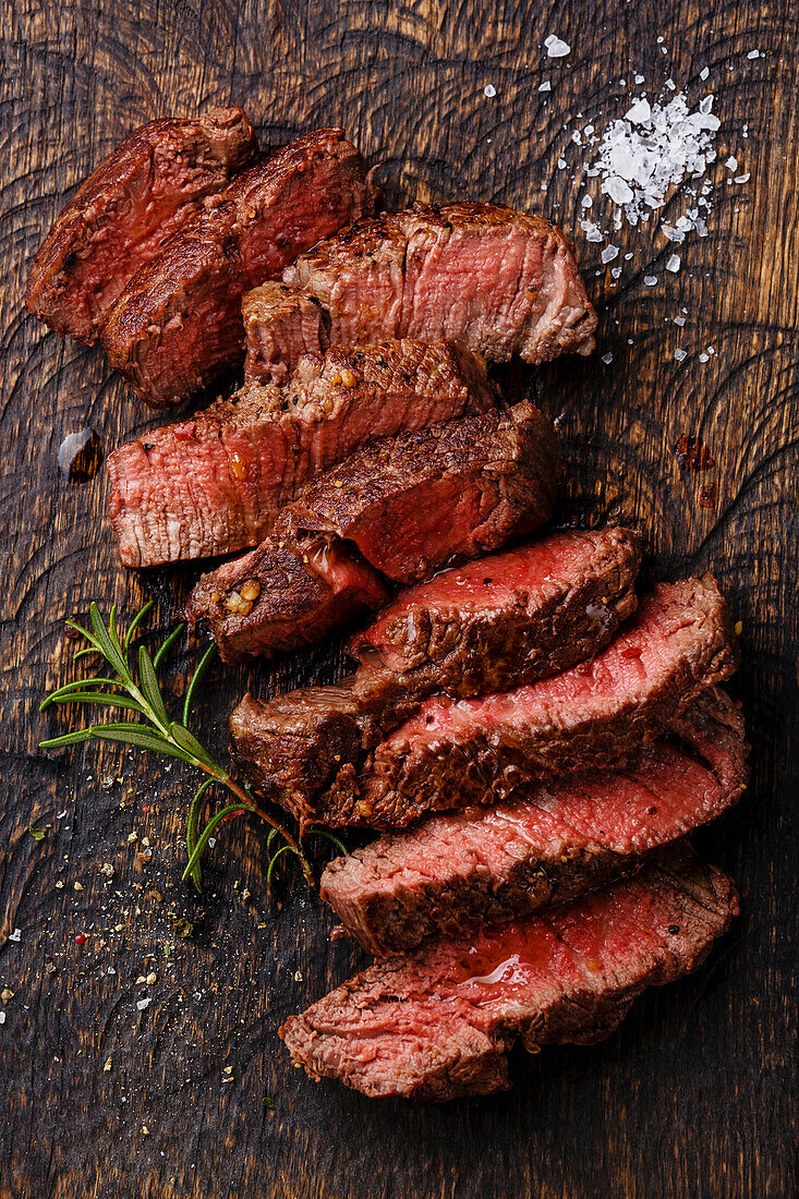 Sliced, medium-grilled beef steak on a wooden chopping board in the background