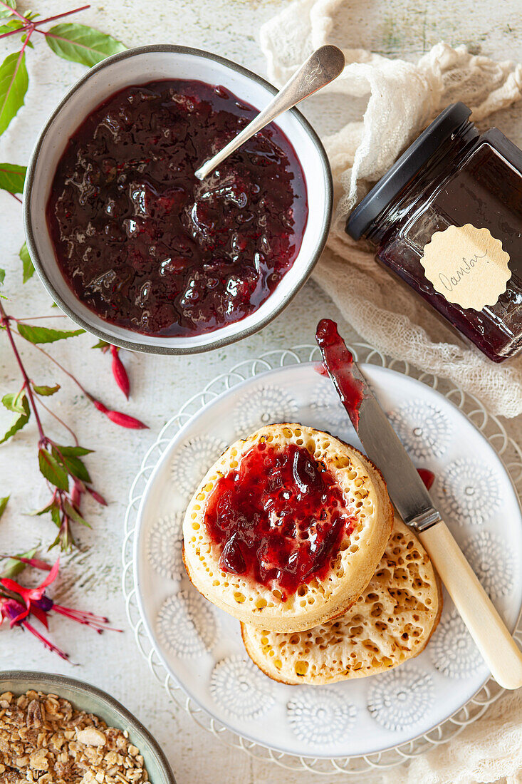 A bowl of damson jam, a jar of homemade jam and jam spread on toasted crumpets.